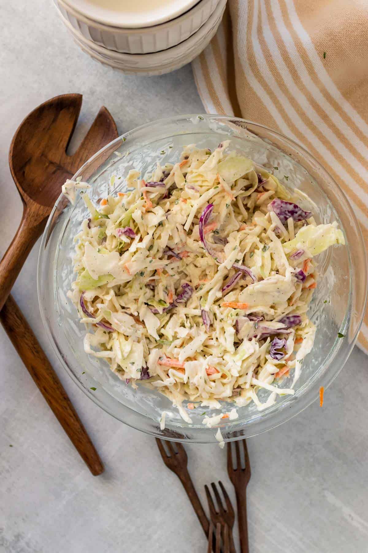 Low carb coleslaw in a large glass bowl next to wooden serving utensils, as seen from above