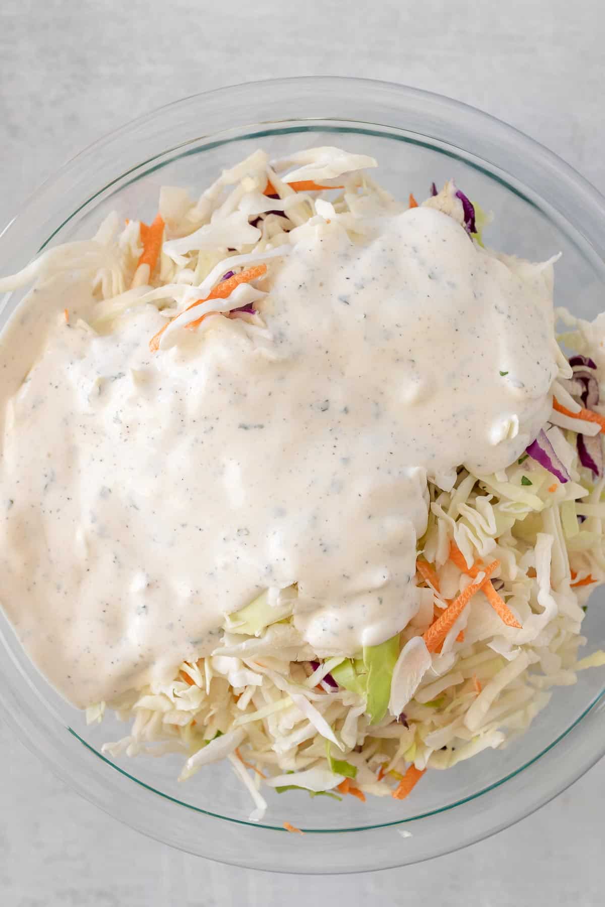 Sauce poured over the coleslaw mixture in a large glass bowl, as seen from above