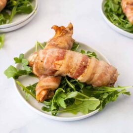 Two bacon wrapped chicken tenders over fresh greens on a white plate