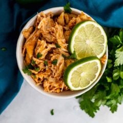 Overhead view of Instant Pot salsa chicken in a white bowl with cilantro and lime wedge garnishes