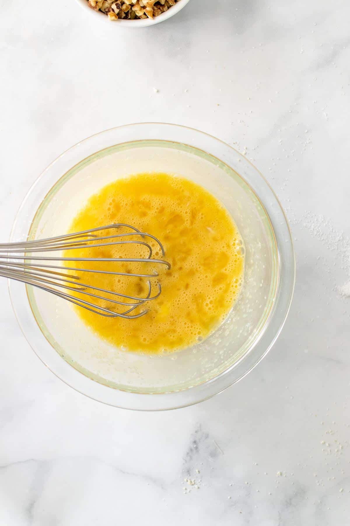 Eggs, sweetener, and vanilla extract in a glass bowl with a whisk, beaten together