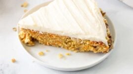 A slice of keto carrot cake on a white plate next to a serving utensil