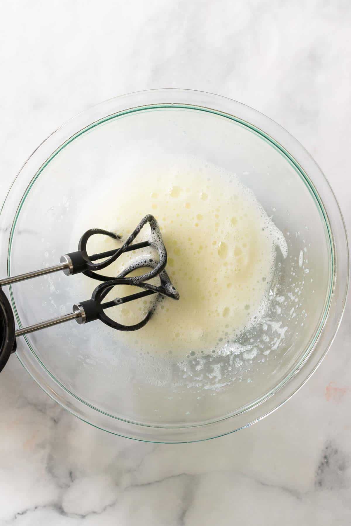 Slightly frothed egg whites in a glass bowl with an electric mixer