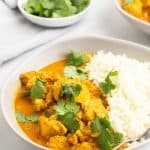 Closeup of chicken curry in a white bowl, garnished with cilantro and served with cauliflower rice