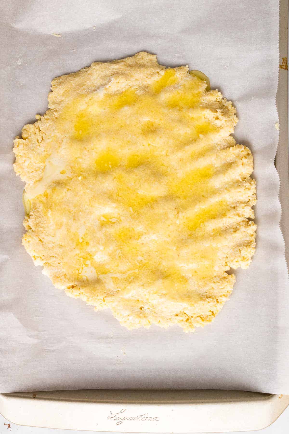 Melted butter spread over the dough on parchment paper, as seen from above