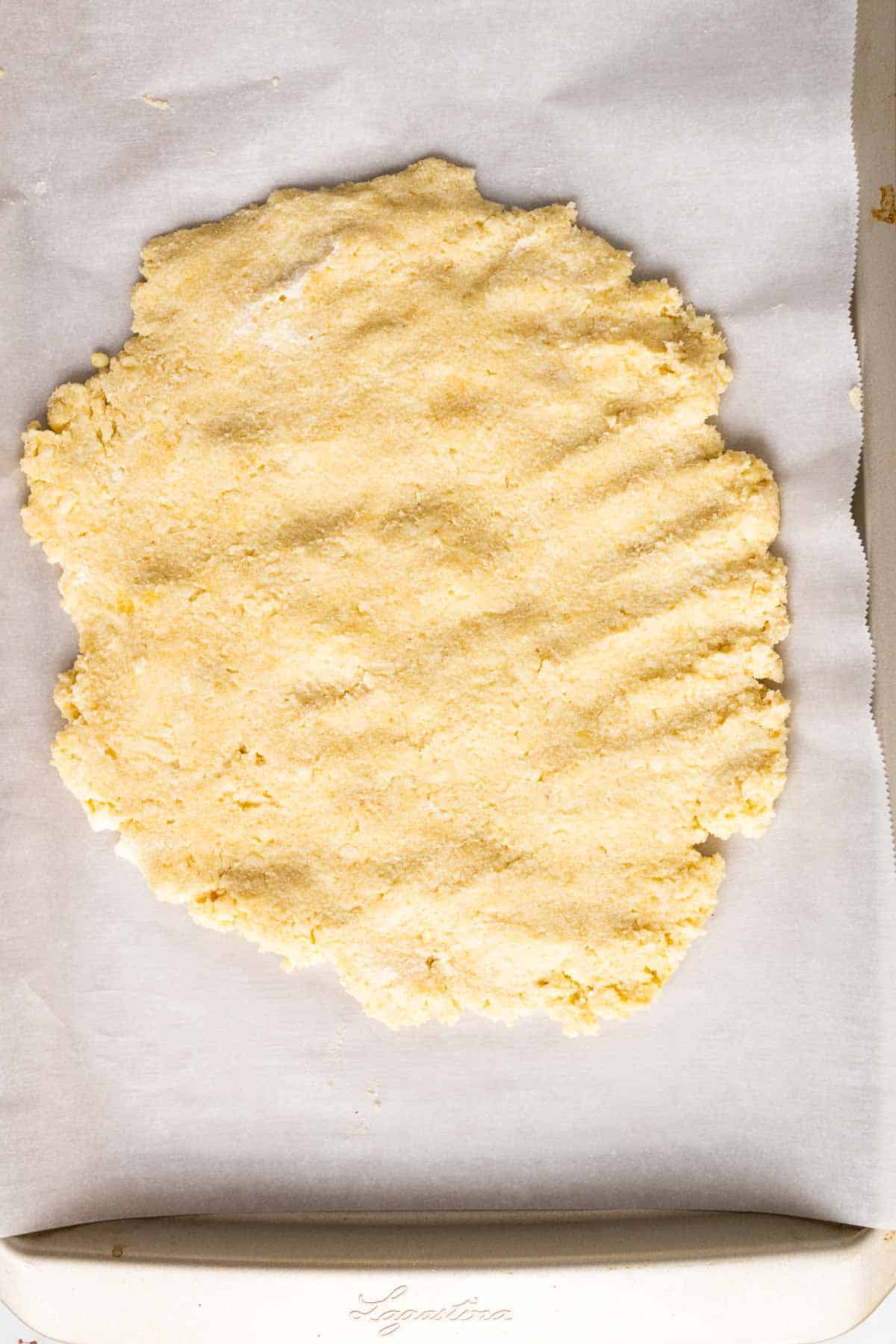 Dough flattened into a rough circle on a baking sheet lined with parchment paper, as seen from above