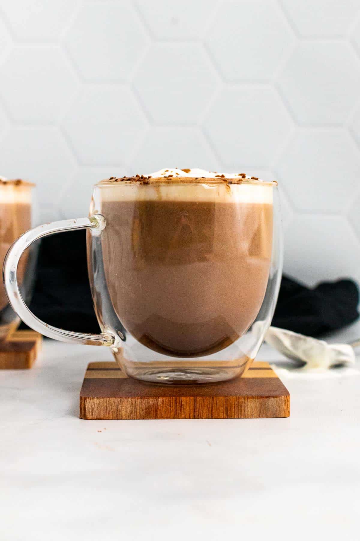 Keto hot chocolate in a clear plastic mug, topped with whipped cream and cocoa powder