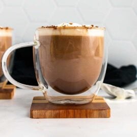 Keto hot chocolate in a clear plastic mug, topped with whipped cream and cocoa powder