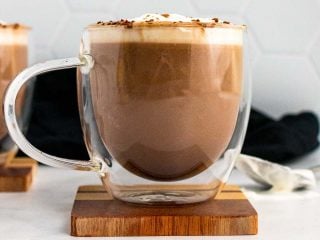 Keto hot chocolate in a clear plastic mug, topped with whipped cream and cocoa powder