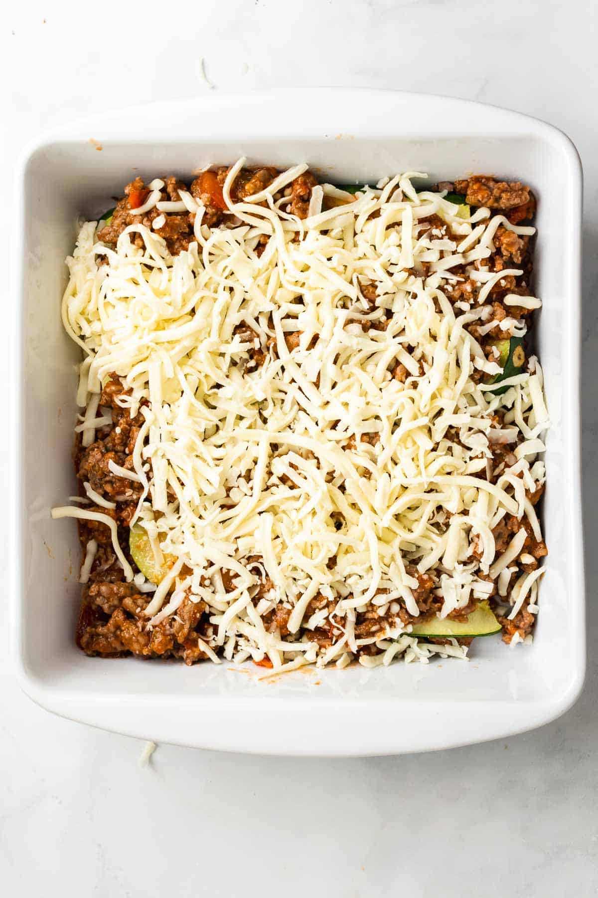 Assembling the lasagna with mozzarella cheese over zucchini slices and the ground beef sauce in a baking pan, as seen from above