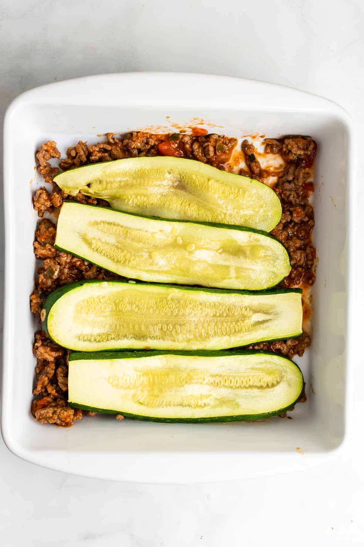Four zucchini slices layered onto the ground beef and tomato sauce mixture in a baking dish