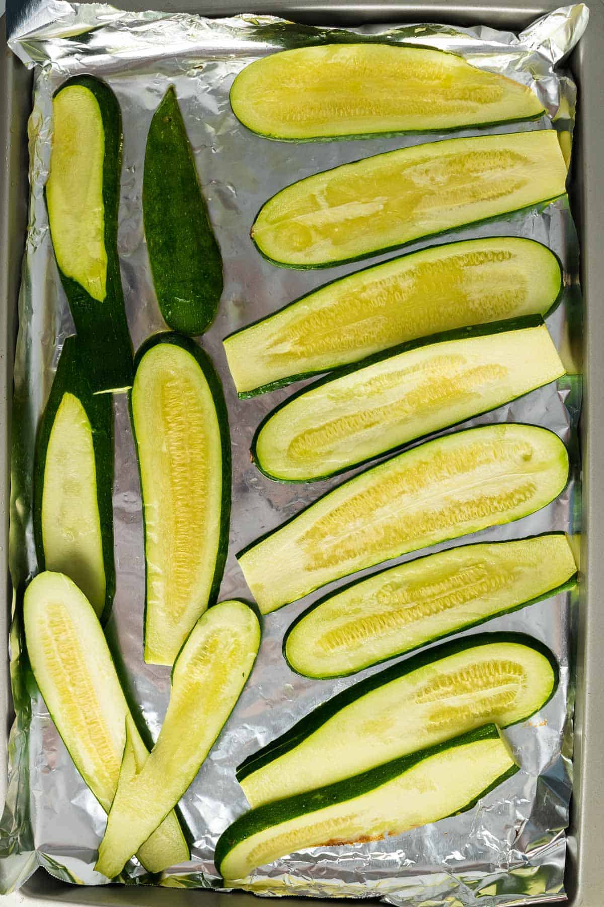 Cooked zucchini slices on a baking sheet lined with foil, as seen from above