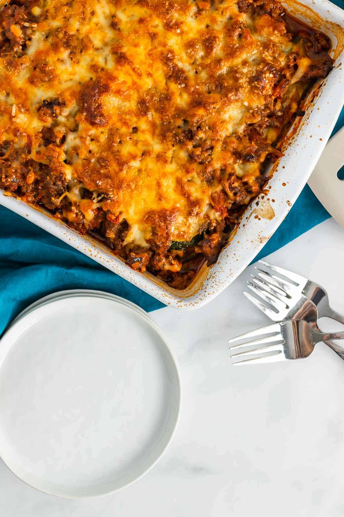 Fully baked lasagna in a baking dish next to an empty plate and two forks