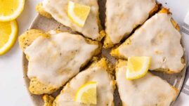Six slices of keto scones on a serving tray topped with lemon glaze and quartered lemon slices, as seen from above