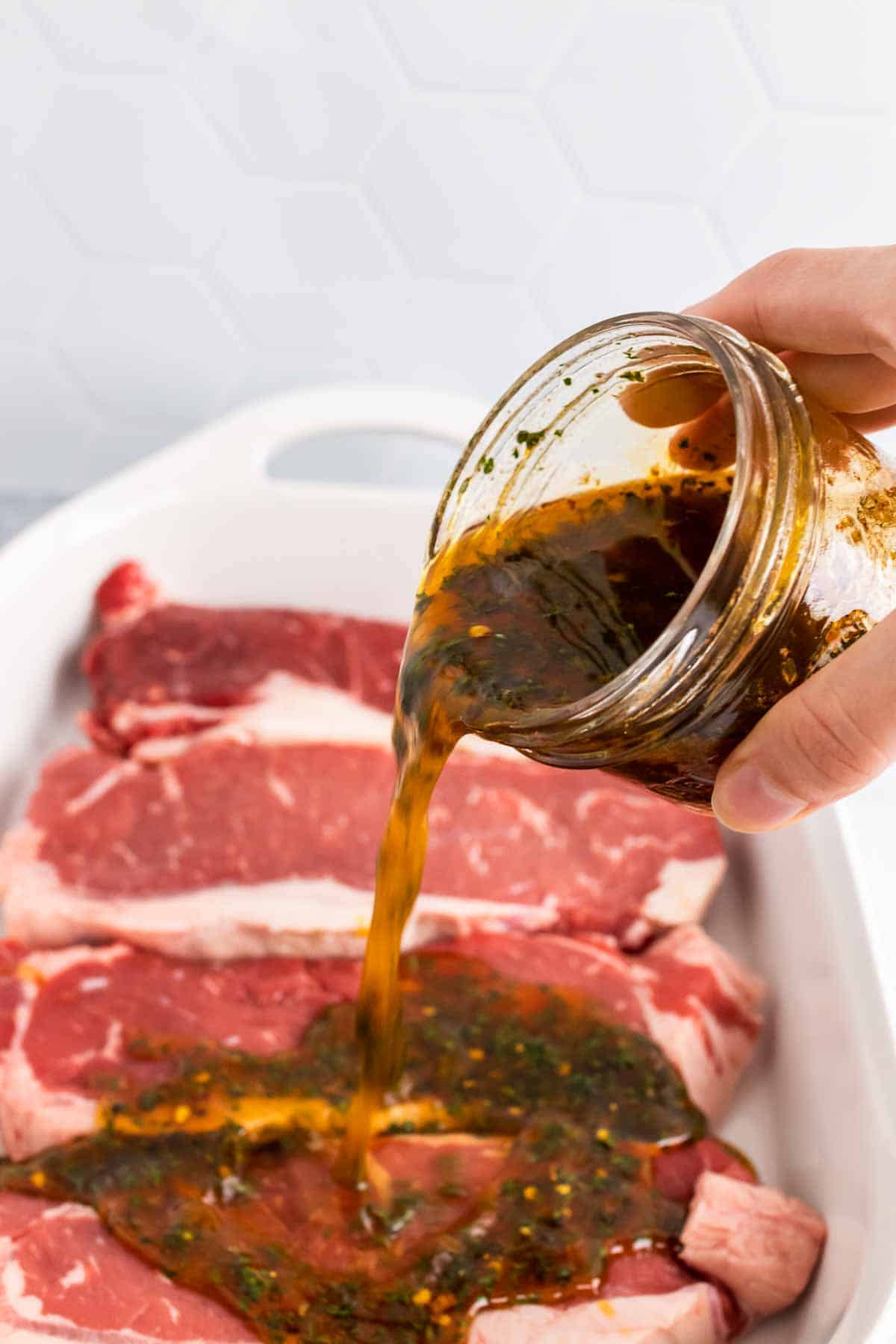 Pouring marinade over four steaks in a large dish