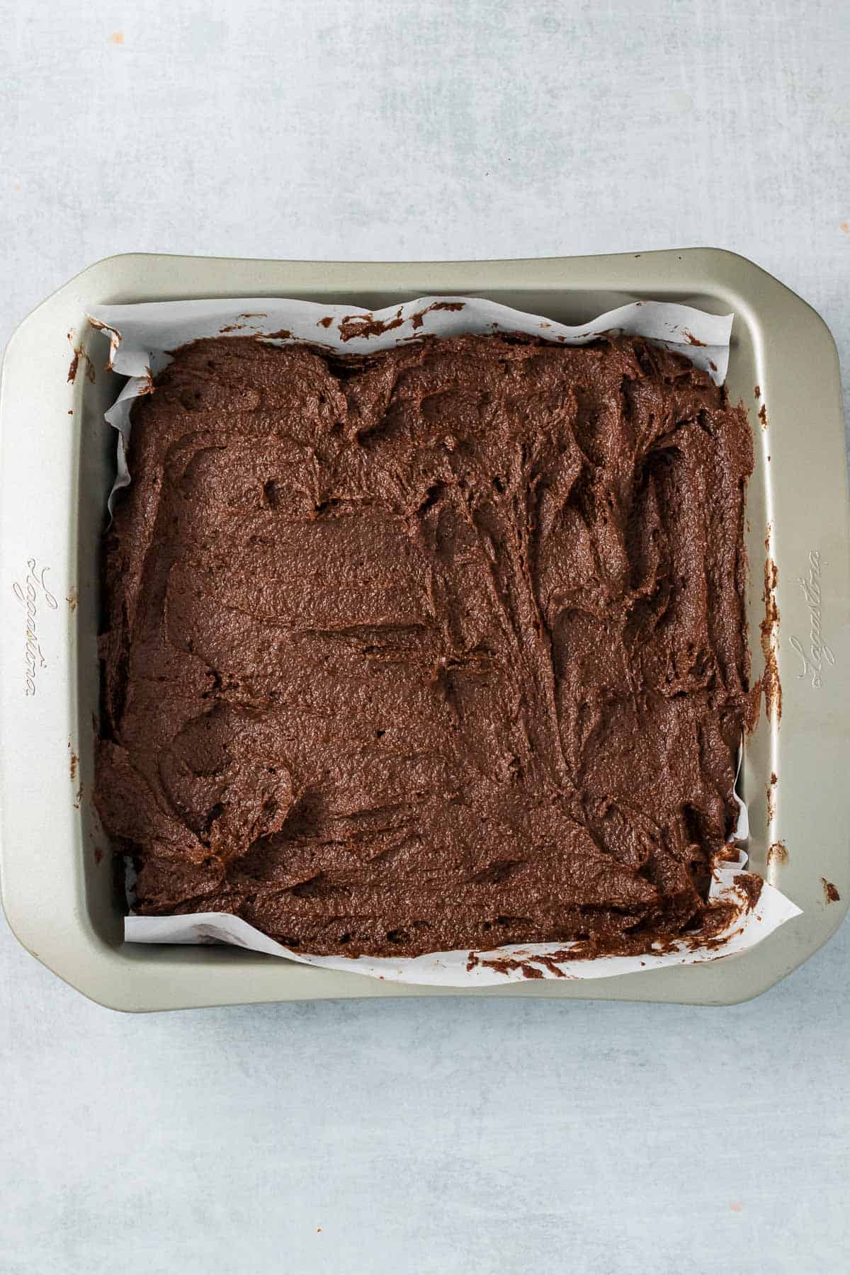 Brownie batter in a square baking dish over parchment paper, ready to bake