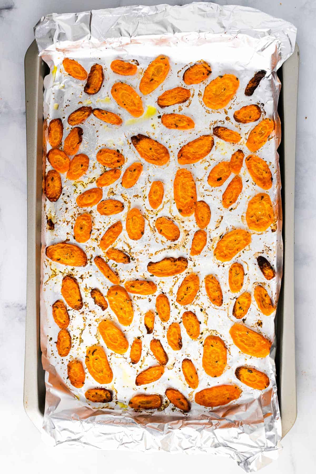 Roasted carrot slices that have finished cooking on a baking sheet covered in foil, as seen from above