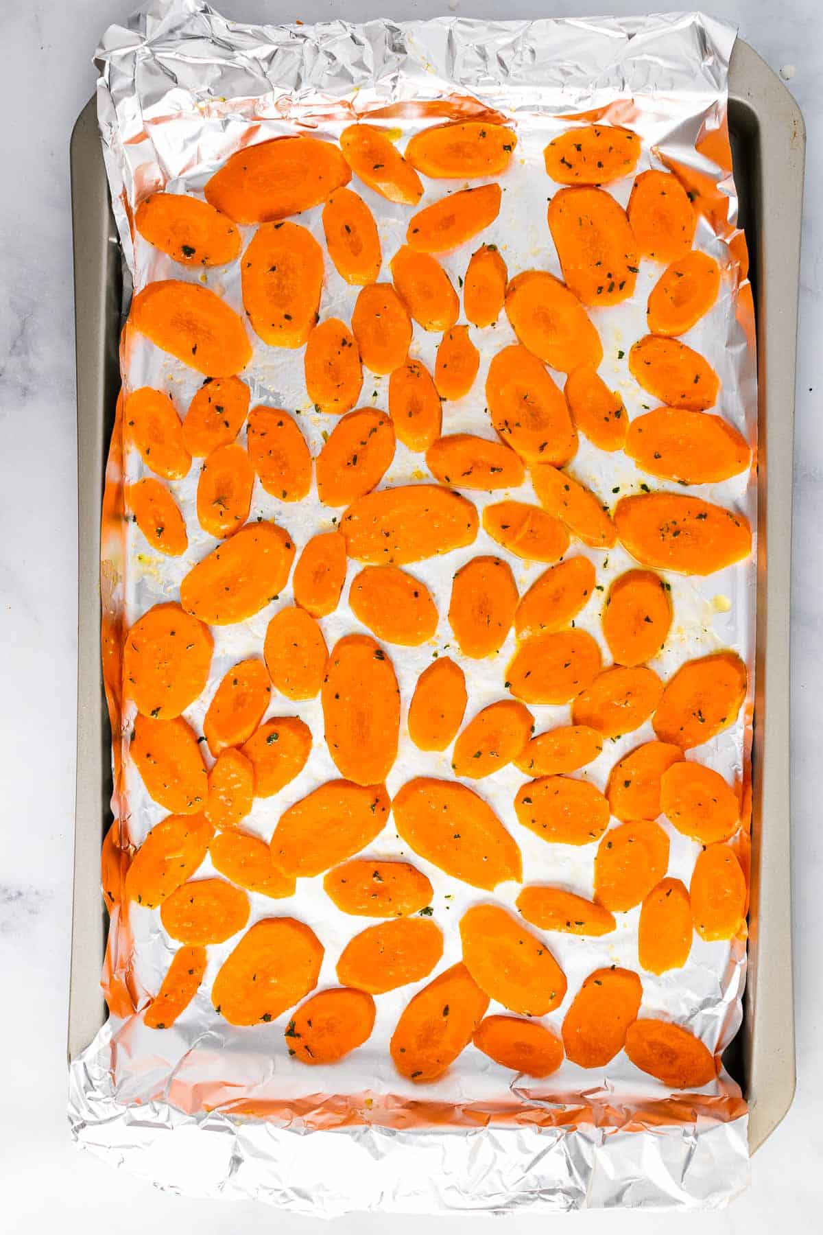 Carrot slices arranged on a baking sheet covered in tin foil, ready to be baked