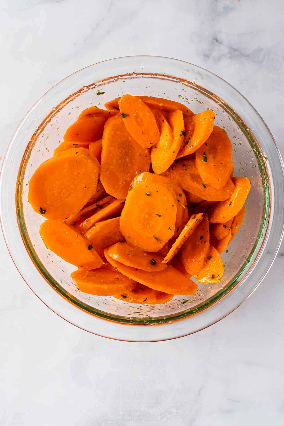 Carrot slices in a glass bowl tossed with oil and spices