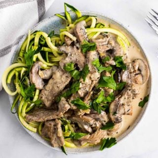 Overhead view of keto beef stroganoff served over zoodles on a white plate and garnished with fresh parsley