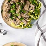 Overhead view of two plates of beef stroganoff served over zoodles on a white plate and topped with fresh parsley
