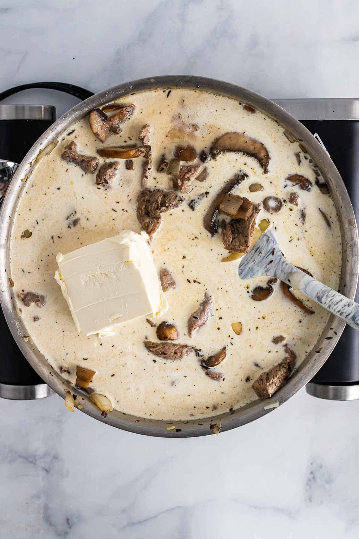 Broth, cream, cream cheese, and coconut aminos added to the mixture in the pan, as seen from above