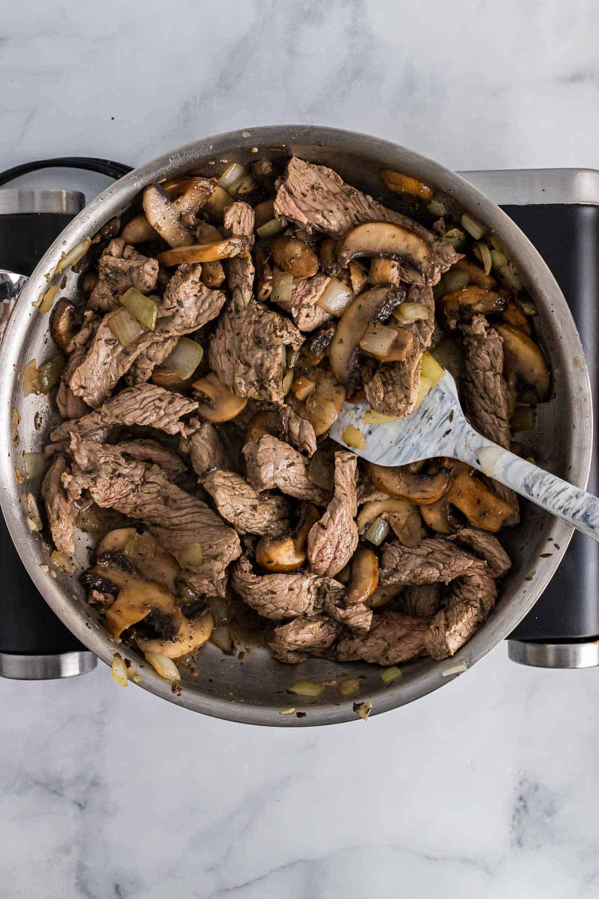 Cooked steak mixed in with the mushroom and onion mixture in the pan, as seen from above