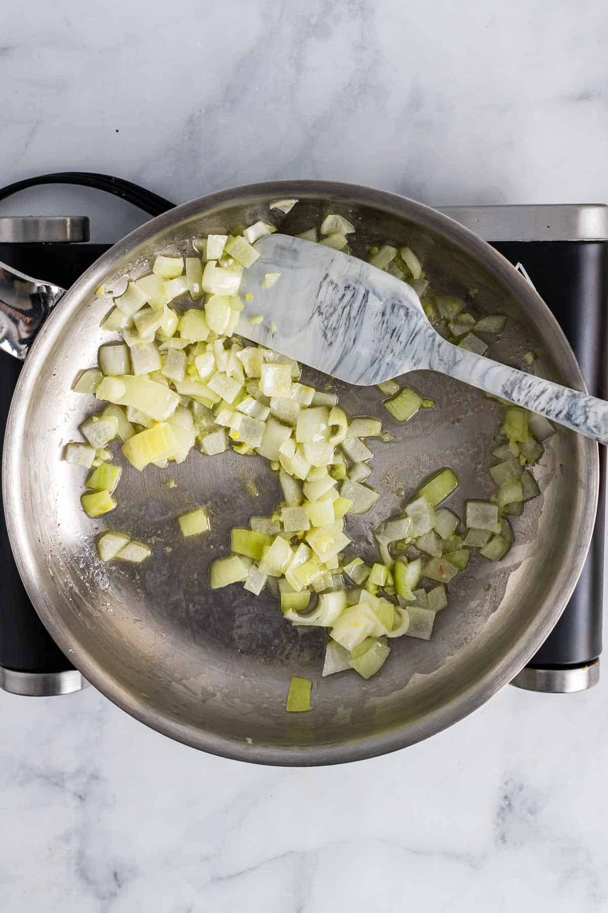Onion, garlic, and butter cooking in a saute pan, as seen from above