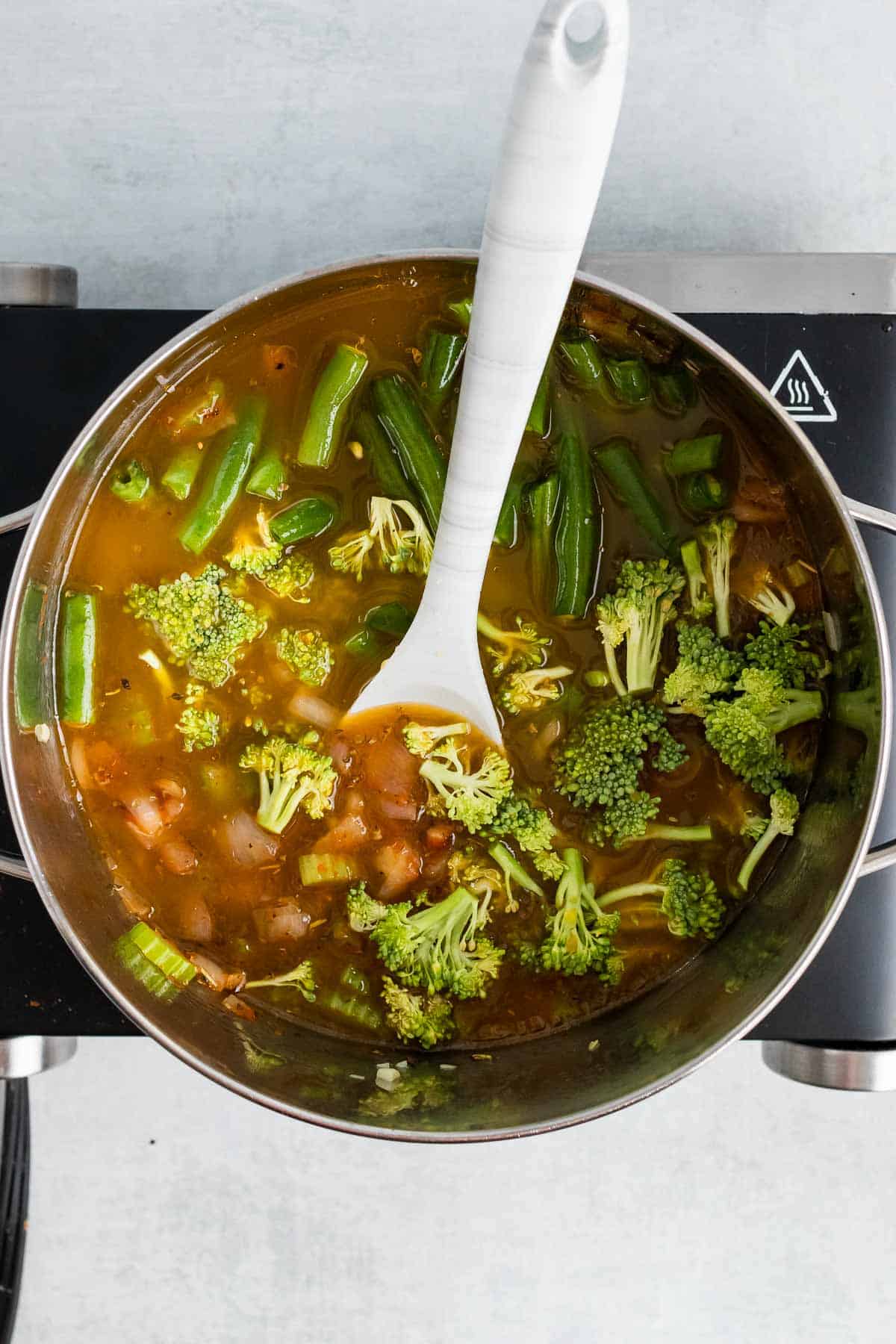 Vegetable stock, broccoli, and green beans added to the sauce pan, as seen from above