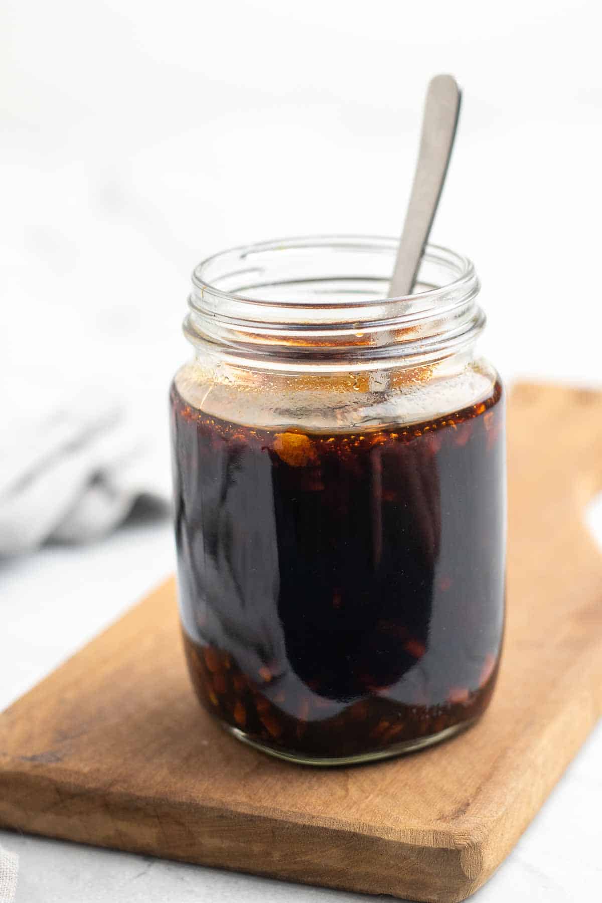 Sugar free teriyaki sauce in a glass mason jar with a metal spoon on a wooden serving tray