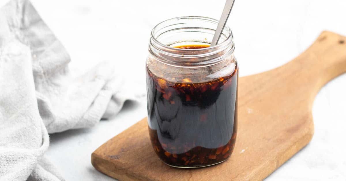 Sugar free teriyaki sauce in a glass mason jar with a metal spoon on top of a wooden serving tray