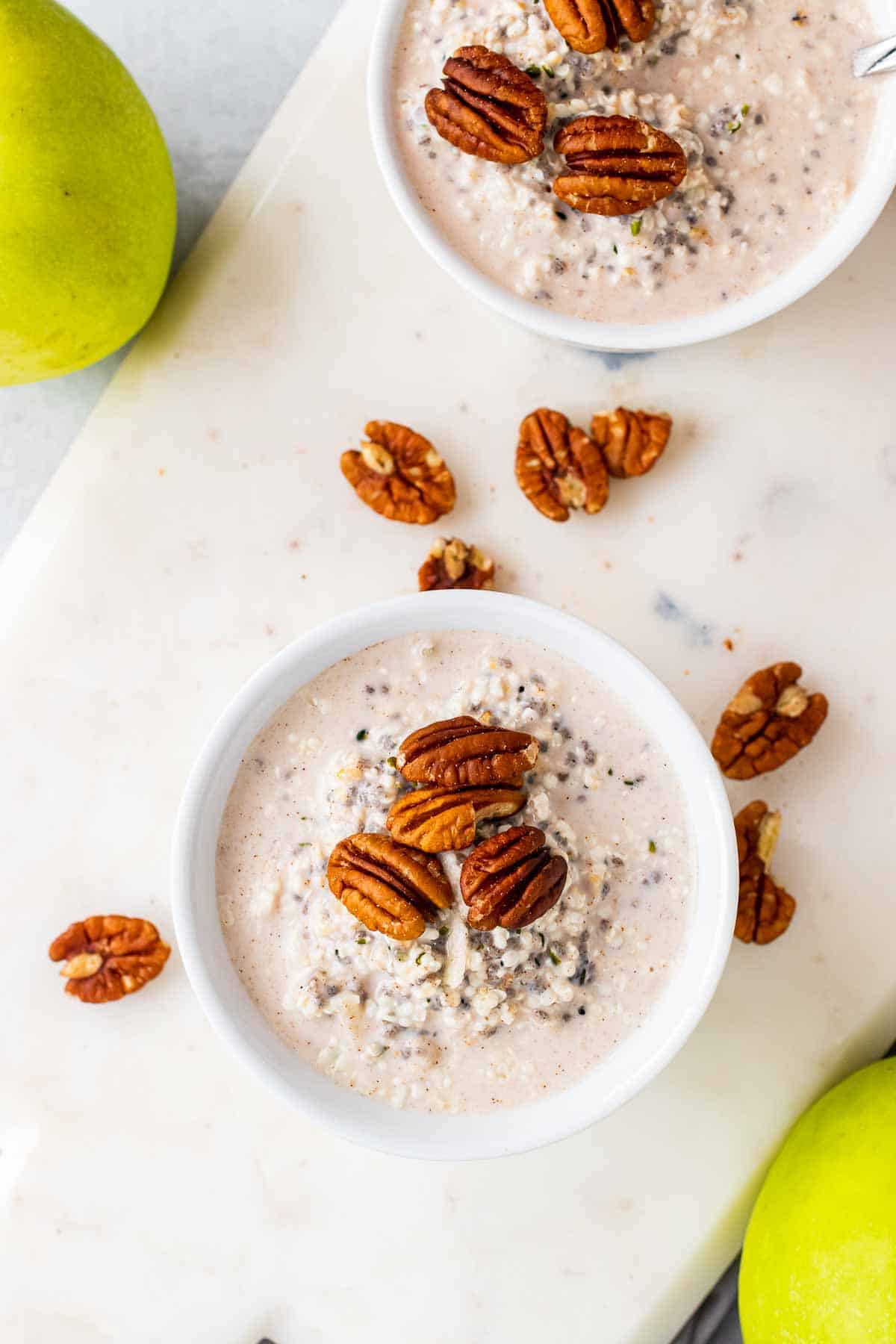 Finished oats in two white bowls topped with pecans on a white serving tray