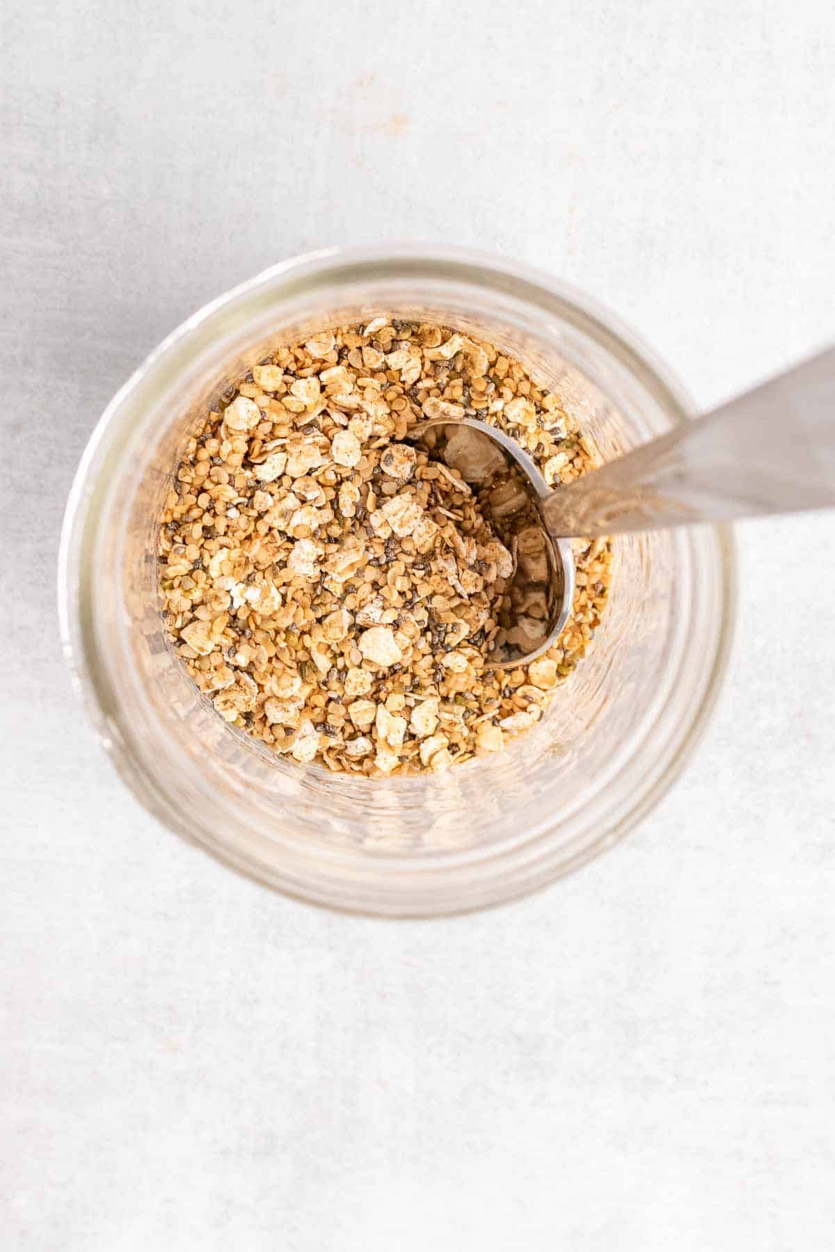 Hemp hearts, oats, chia seeds, and cinnamon in a jar with a spoon, as seen from above