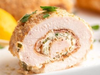 Close-up of a slice of low carb chicken rollatini on a white plate, topped with chopped sage