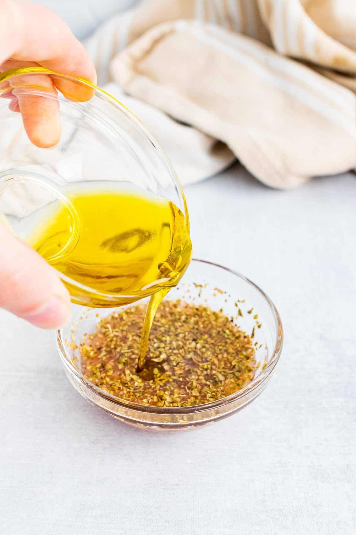 Hand pouring olive oil into the dressing from a glass.