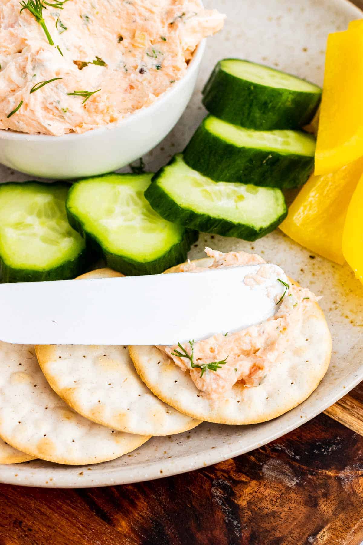 Knife putting salmon spread on a cracker
