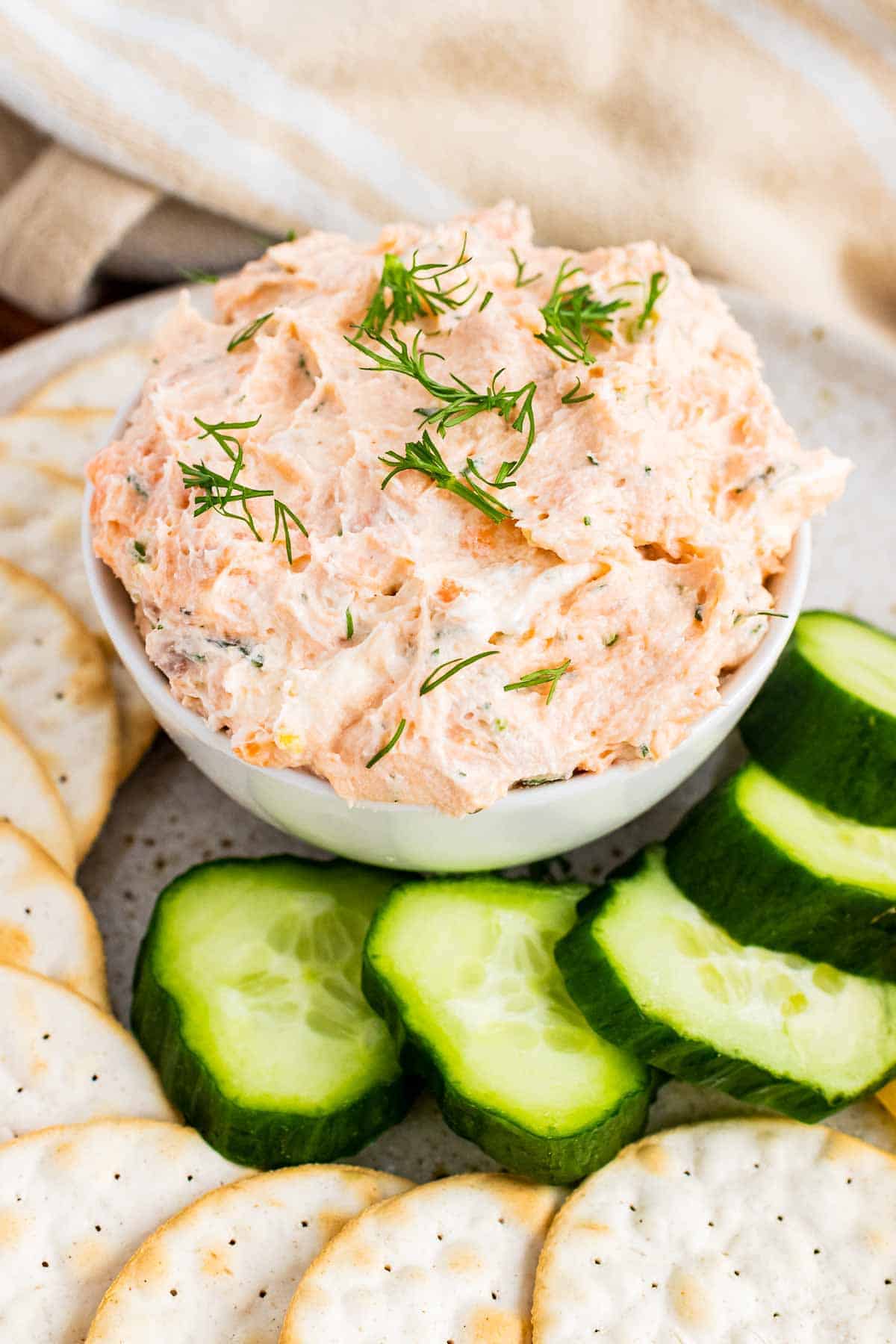 Bowl of smoked salmon spread with crackers and cucumbers