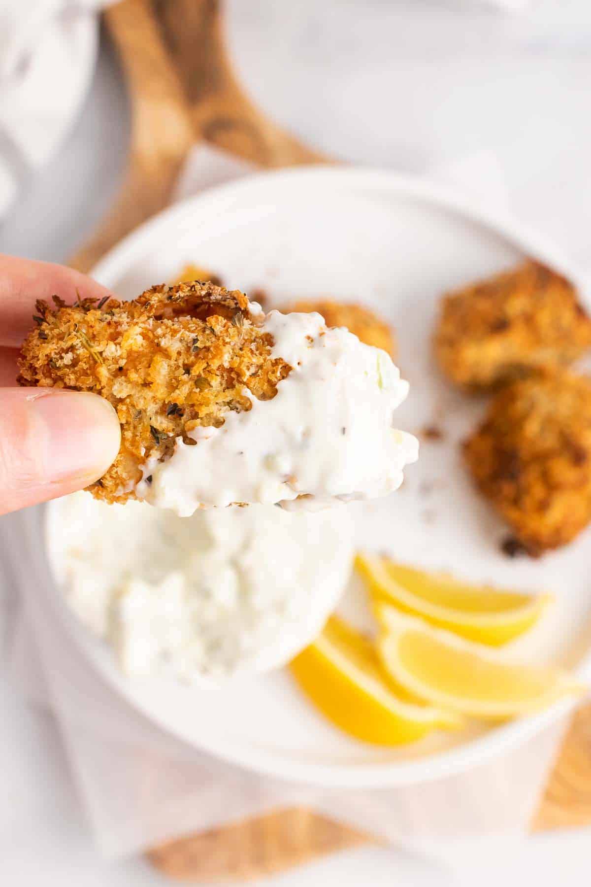 Hand holding chicken tender with tartar sauce over plate