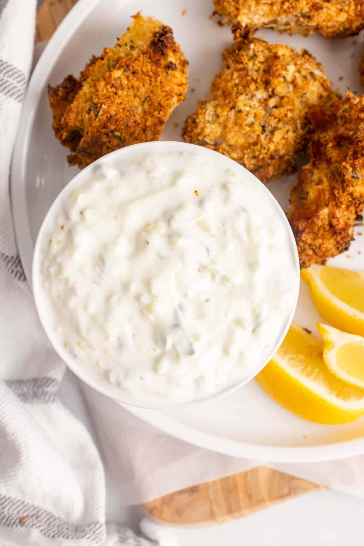 Bowl of light tartar sauce surrounded by crispy chicken tenders 