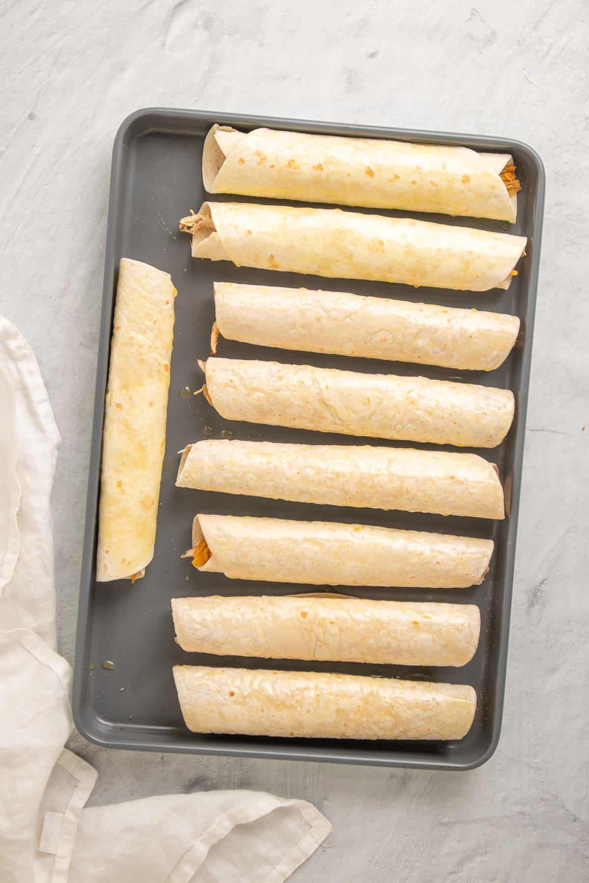Nine taquitos rolled and placed on a baking tray, ready to go in the oven