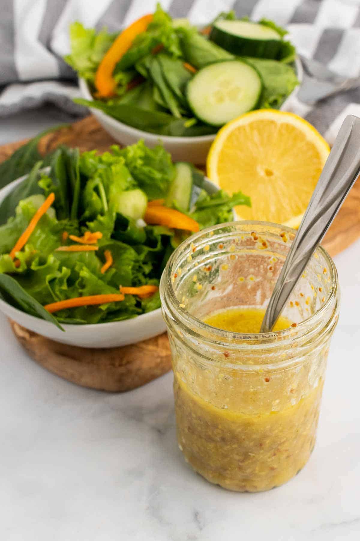Glass jar of lemon vinaigrette in front of salad bowl