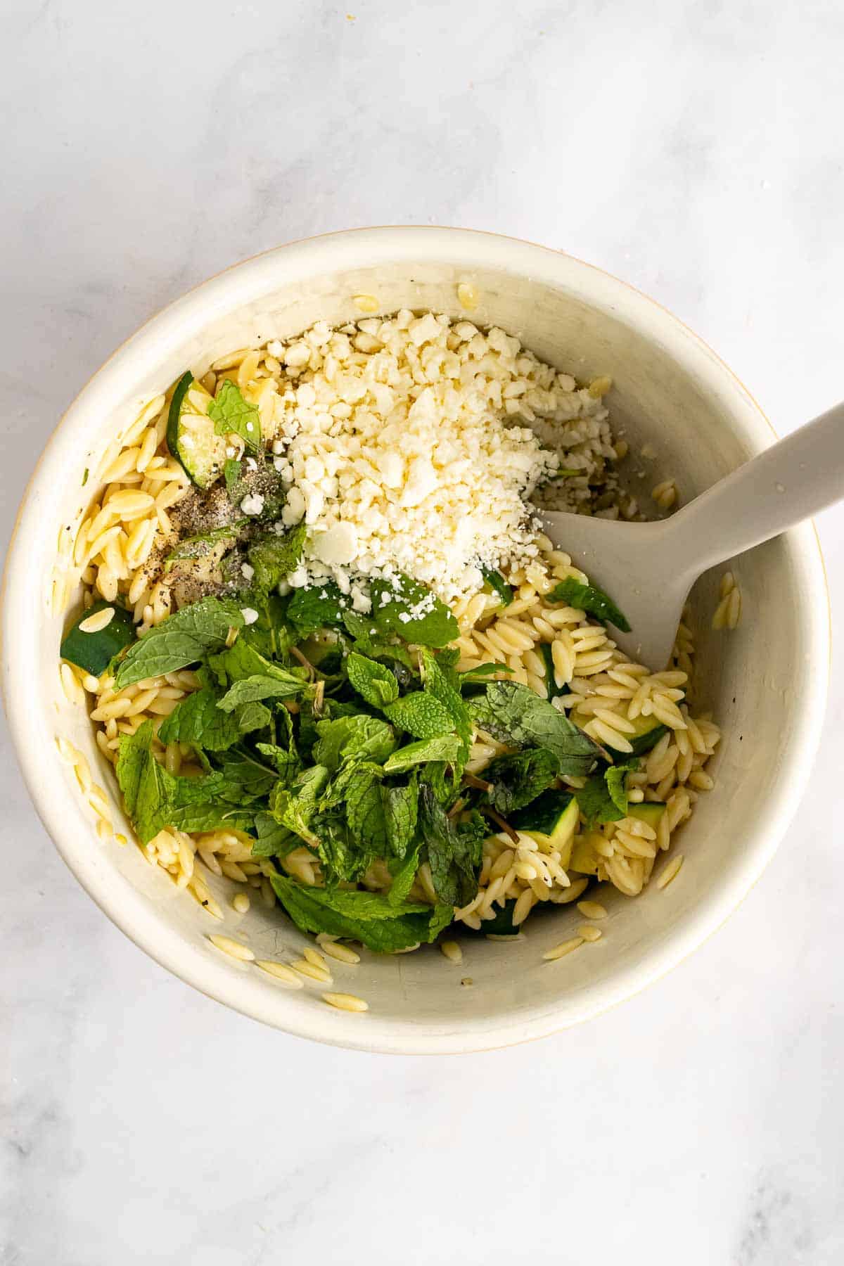 Bowl of orzo zucchini salad with faeta and mint on top