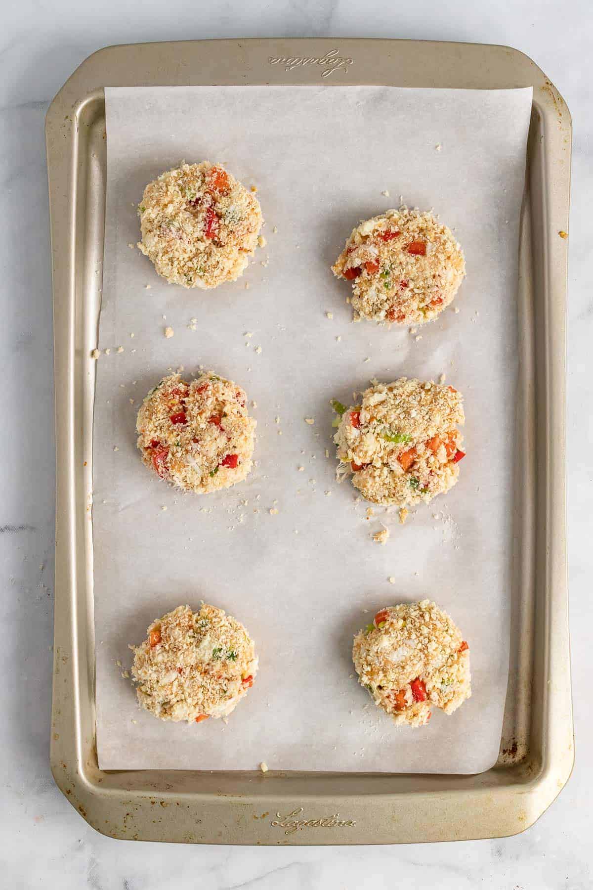 Six crab cakes on a baking tray, ready to go in the oven