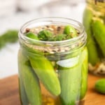 A glass jar of cucumbers in the pickling mixture on a wooden serving tray