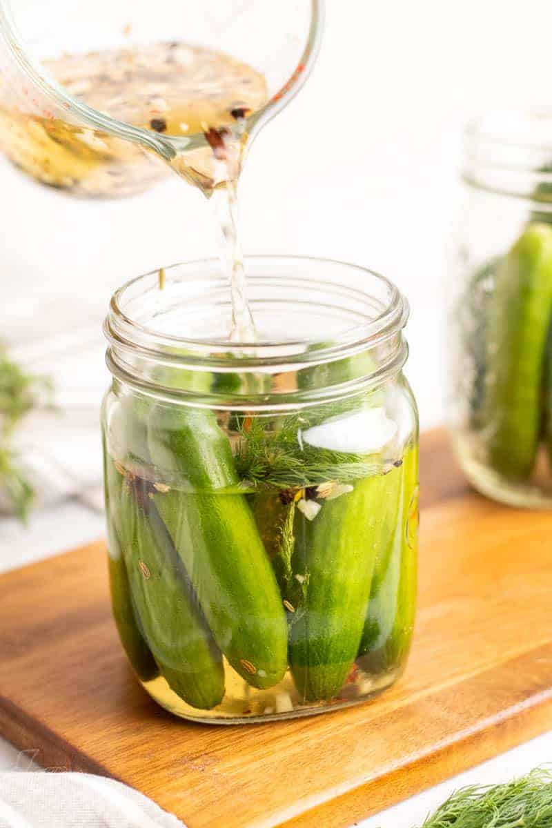 Pouring the pickling mixture into the glass jar with the cucumbers