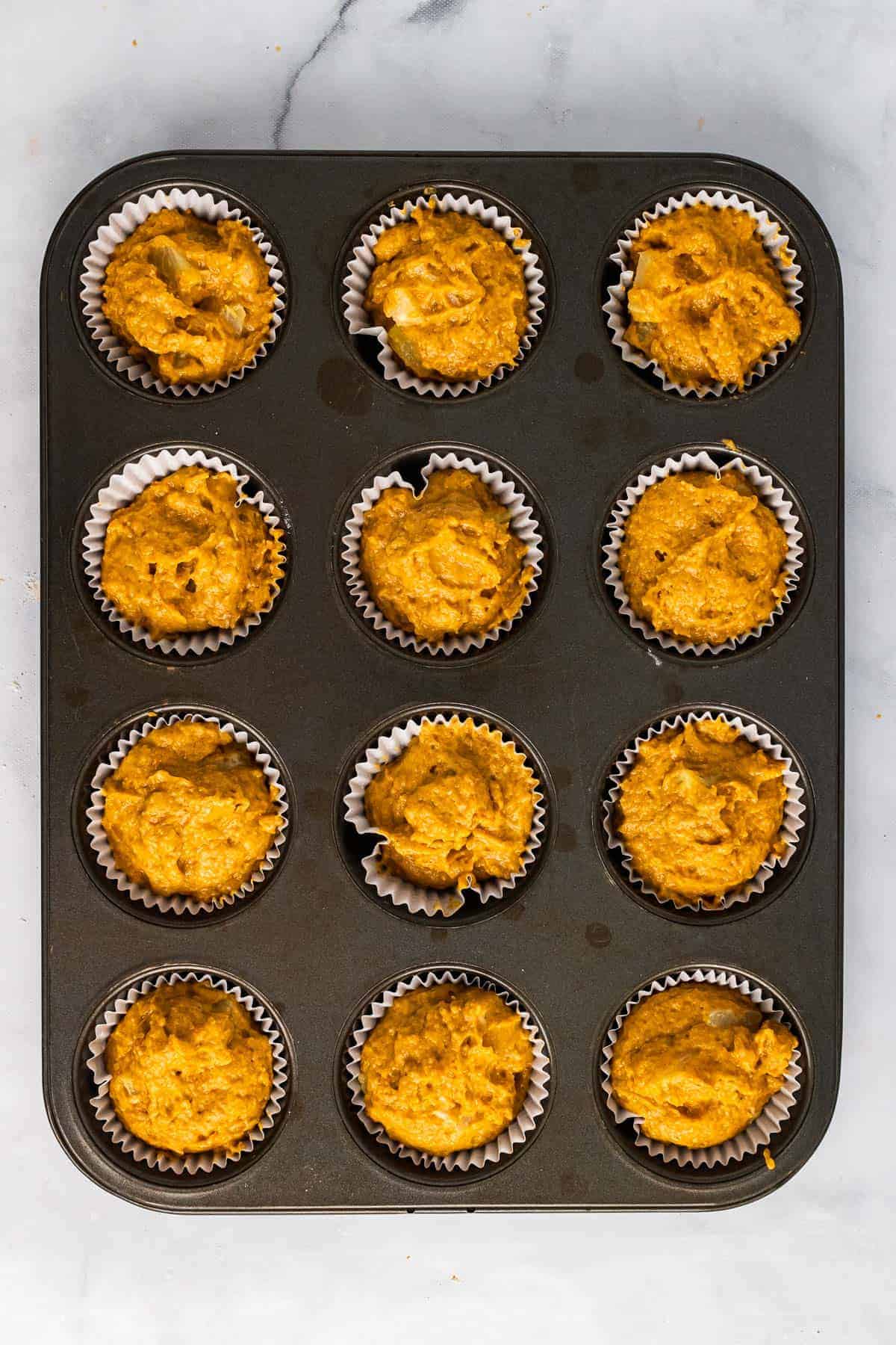 Batter distributed evenly into 12 muffin cups in a tray, as seen from above