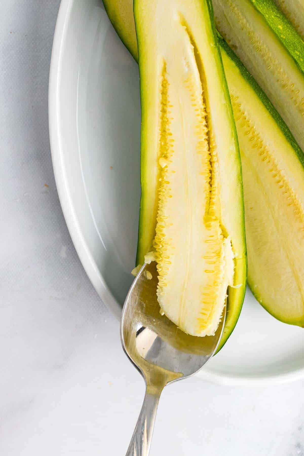 Using a spoon to scoop the flesh from the inside of the zucchini half