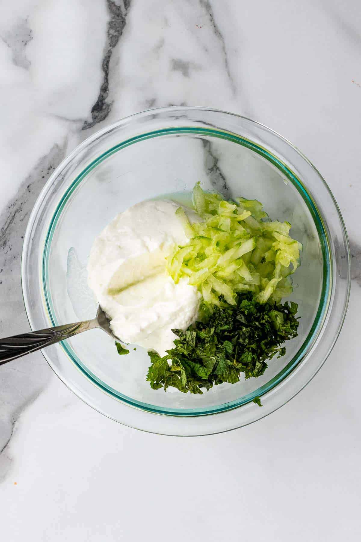 Cucumber, mint, cilantro, and yogurt in a glass bowl