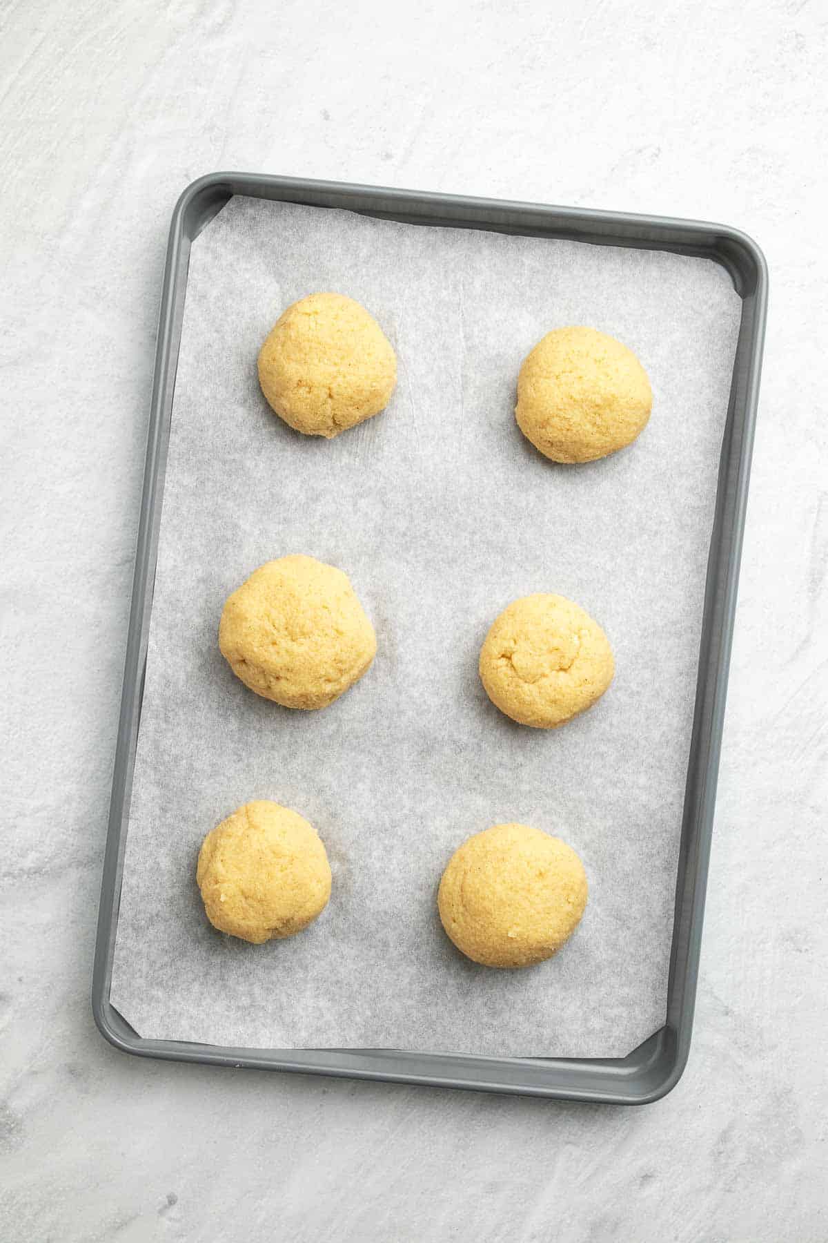 Six dough balls on a baking sheet lined with parchment paper, as seen from above