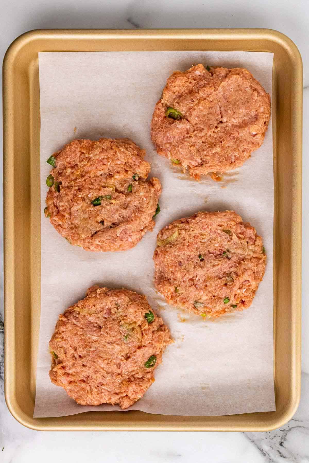 Four burger patties on a baking sheet